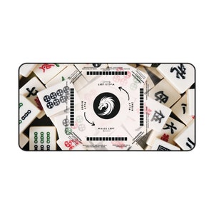 May include: A rectangular Mahjong game mat with a black border, featuring scattered ivory-colored tiles. A central graphic displays a white dragon within a black circle, with directional arrows and text indicating gameplay. The tiles have red, green, and black markings.