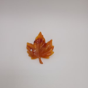 May include: A brown and orange maple leaf with a small clear rhinestone in the center.