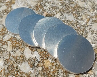 May include: Five silver-colored metal discs stacked on top of each other on a rough, gray, and brown surface.