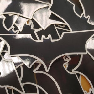 May include: A pile of black and white Batman logo stickers. The stickers are glossy and have a white outline.
