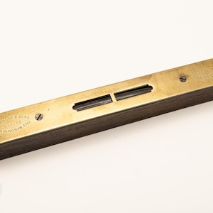 May include: A vintage spirit level featuring a dark wood base and a brass top plate. The brass plate is engraved with the text Rabone & Sons Makers Birmingham Eng and Warranted Correct. It includes a central glass vial for leveling measurements.