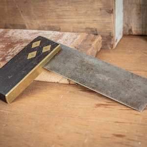 Peut inclure: Une équerre en bois et en laiton vintage avec une lame en métal. La lame est légèrement rouillée et le manche en bois a une finition foncée. Le manche a quatre incrustations en laiton en forme de diamants.