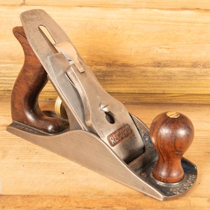 Könnte beinhalten: Ein Vintage-Metall-Handhobel mit Holzgriff und Knauf. Der Hobel hat eine silberne Klinge und einen braunen Holzgriff und Knauf. Das Wort "RECORD" ist auf der Seite des Hobels sichtbar. Das Werkzeug ist für die Holzbearbeitung.