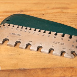 May include: A white ceramic mug with a black handle and the text "But First, Coffee" in a bold, black font. The mug is set against a blurred background, suggesting a cozy setting.