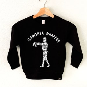 Puede incluir: Sudadera negra de manga larga con un gráfico blanco de una momie y el texto "Gangsta Wrapper".