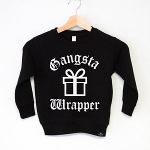 Puede incluir: Sudadera negra con texto blanco que dice "Gangsta Wrapper" y un gráfico de caja de regalo blanco.