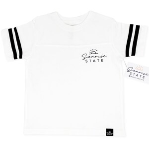 May include: White t-shirt with black stripes on the sleeves and a black logo that says "Sunrise State". The shirt has a tag with the same logo and the Instagram handle @sunrisestate.