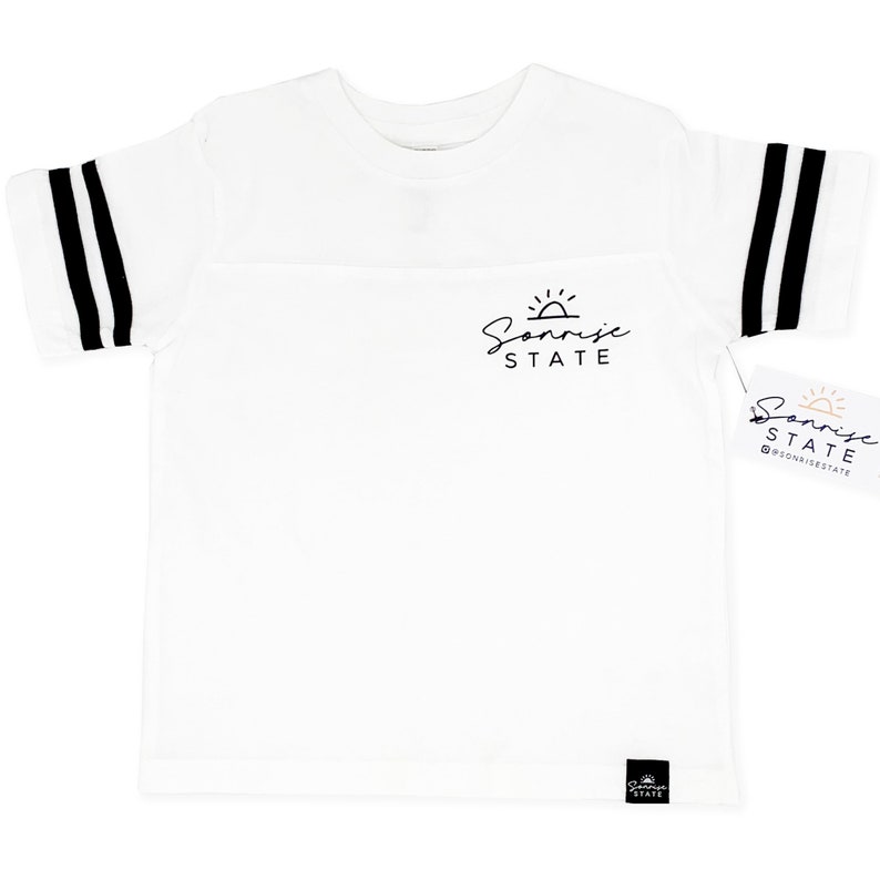May include: White t-shirt with black stripes on the sleeves and a black logo that says "Sunrise State". The shirt has a tag with the same logo and the Instagram handle @sunrisestate.
