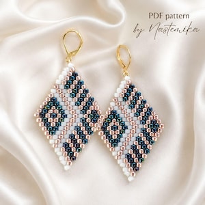 May include: A pair of diamond-shaped beaded earrings featuring a geometric pattern of white, metallic rose gold, and iridescent dark blue glass beads. The earrings are attached to gold-tone lever-back hooks. The text PDF pattern by Nastemika is visible.