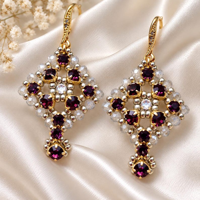 May include: A pair of dangle earrings featuring a diamond-shaped lattice design crafted from silver-toned beads and deep purple round crystals. Each earring is suspended from a gold-toned hook with a small clear crystal accent at the top.