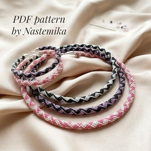 Pode incluir: Três colares circulares de contas com um padrão em ziguezague em preto, branco e tons de rosa. As peças de joalharia são feitas de contas pequenas e uniformes. O texto no canto superior esquerdo diz: PDF pattern by Nastemika.