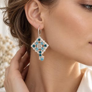 May include: A silver leverback earring featuring a diamond-shaped arrangement of small white pearls and round faceted crystals in alternating shades of light blue and dark teal, with a single dangling crystal accent at the bottom point.