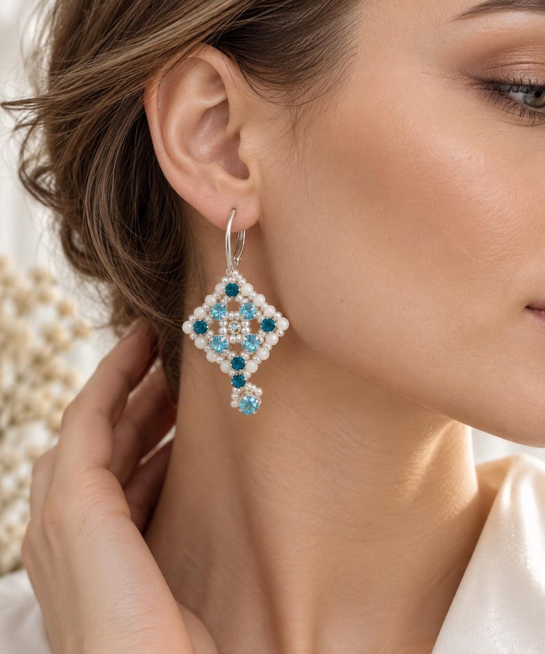 May include: A silver leverback earring featuring a diamond-shaped arrangement of small white pearls and round faceted crystals in alternating shades of light blue and dark teal, with a single dangling crystal accent at the bottom point.