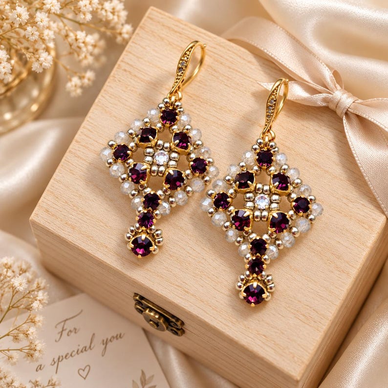 May include: A pair of dangle earrings featuring a diamond-shaped lattice design crafted from deep purple faceted crystals and small iridescent white beads. The earrings are finished with gold-toned metal hooks and a single purple crystal drop.