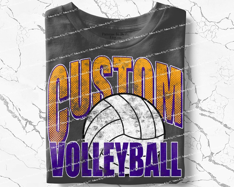 May include: Dark gray t-shirt featuring a volleyball design. The shirt has the word "CUSTOM" in orange and purple, with a distressed dot pattern. Below the volleyball is the word "VOLLEYBALL" in purple. The shirt is folded.