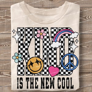 May include: A white t-shirt with a black and white checkered design that spells out "KIND IS THE NEW COOL". The design includes a smiley face, a peace sign, a heart, and flowers.