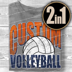 May include: Gray t-shirt with a volleyball graphic. The shirt features the words "CUSTOM VOLLEYBALL" in orange and navy blue, with a volleyball in the center. A black and gold circle with "2 in 1" is in the upper right corner.