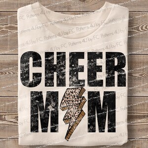 Op de afbeelding: Een wit T-shirt met de tekst "CHEER MOM" in zwart met een verweerde look. Een bliksemgraphic in luipaardprint bevindt zich in het midden van het shirt.