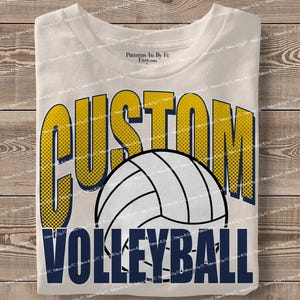 May include: Cream-colored t-shirt with the words "CUSTOM VOLLEYBALL" in a bold, two-tone design. The word "CUSTOM" is in yellow with a dotted pattern, and "VOLLEYBALL" is in navy blue. A white volleyball graphic is centered.