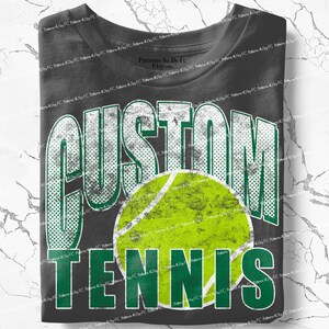 Puede incluir: Una camiseta gris oscuro con las palabras "CUSTOM TENNIS" en blanco y verde, con un gr&aacute;fico de pelota de tenis. La camiseta tiene un aspecto desgastado y vintage.