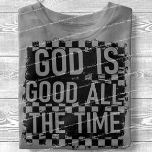 May include: A folded gray t-shirt with the words "GOD IS GOOD ALL THE TIME" in large, black, distressed lettering. The text is set against a checkered background.