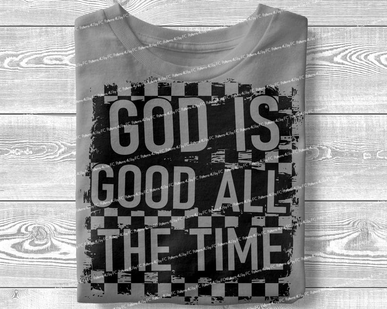 May include: A folded gray t-shirt with the words "GOD IS GOOD ALL THE TIME" in large, black, distressed lettering. The text is set against a checkered background.