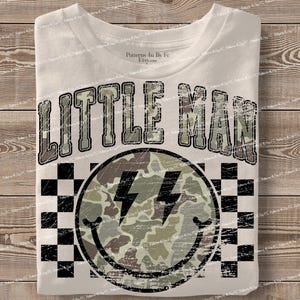 K&ouml;nnte beinhalten: Wei&szlig;es T-Shirt mit dem Text "LITTLE MAN" in einer Camouflage-Schriftart &uuml;ber einem Smiley mit Blitzsymbolen. Der Smiley hat ein Camouflage-Muster und ist von einem schwarz-wei&szlig;en Schachbrettmuster umgeben.