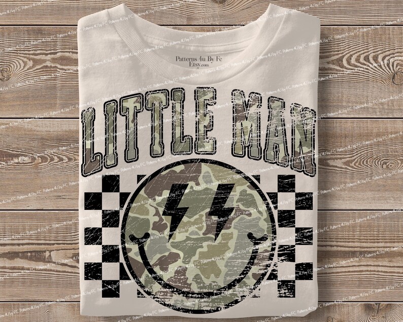 K&ouml;nnte beinhalten: Wei&szlig;es T-Shirt mit dem Text "LITTLE MAN" in einer Camouflage-Schriftart &uuml;ber einem Smiley mit Blitzsymbolen. Der Smiley hat ein Camouflage-Muster und ist von einem schwarz-wei&szlig;en Schachbrettmuster umgeben.