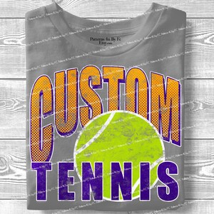 Puede incluir: Camiseta gris con las palabras "CUSTOM TENNIS" en naranja y morado, con un gr&aacute;fico de pelota de tenis. La camiseta tiene un aspecto desgastado y vintage.