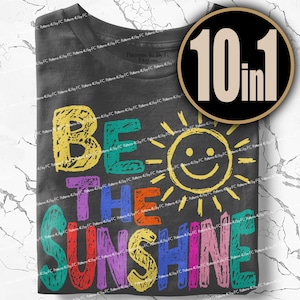 May include: Dark gray t-shirt with the words "BE THE SUNSHINE" in colorful, textured letters. A smiling sun graphic is between "THE" and "SUNSHINE". A black circle with "10 in 1" in white is in the upper right corner.