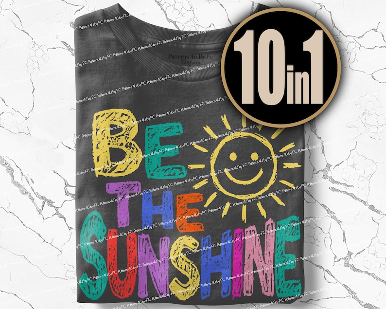 May include: Dark gray t-shirt with the words "BE THE SUNSHINE" in colorful, textured letters. A smiling sun graphic is between "THE" and "SUNSHINE". A black circle with "10 in 1" in white is in the upper right corner.