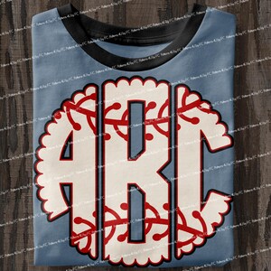 May include: A light blue t-shirt with a white and red monogram design. The monogram is in the shape of a baseball with a scalloped edge.