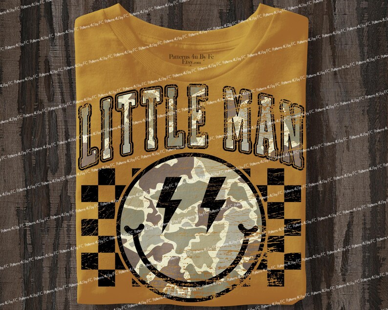 K&ouml;nnte beinhalten: Senfgelbes T-Shirt mit dem Text "LITTLE MAN" in einer verblassten Schriftart. Darunter befindet sich ein Smiley mit Blitzaugen und einem Tarnmuster. Der Hintergrund hat ein schwarz-gelbes Schachbrettmuster.