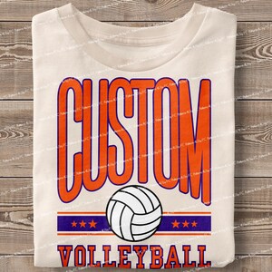 May include: White t-shirt with the text "CUSTOM VOLLEYBALL" in orange and purple. A white volleyball with orange and black details is in the centre of the design.