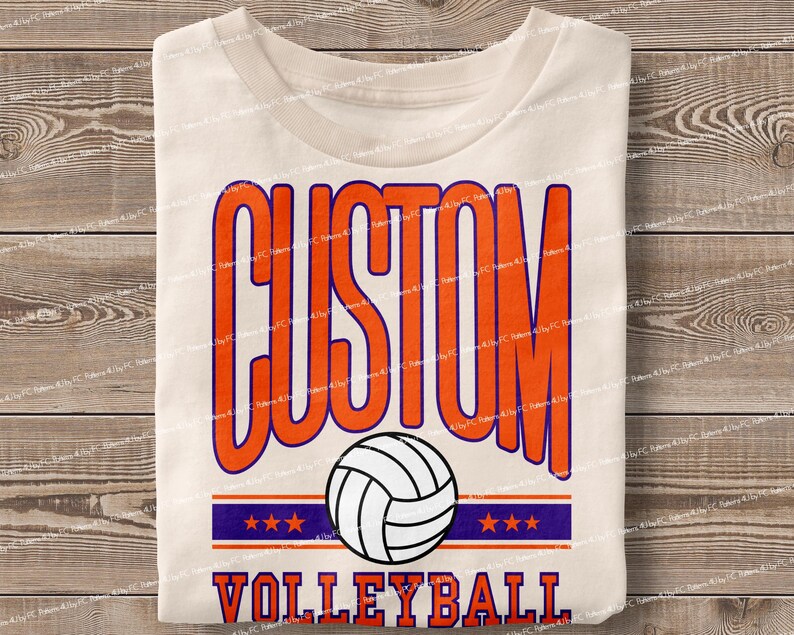 May include: White t-shirt with the text "CUSTOM VOLLEYBALL" in orange and purple. A white volleyball with orange and black details is in the centre of the design.