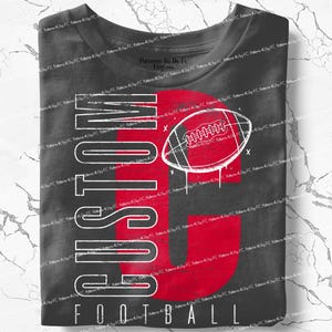 May include: A dark gray t-shirt with a red football graphic and the word "CUSTOM" in white, stacked vertically. The word "FOOTBALL" is printed horizontally at the bottom. A football is in the center of the design.