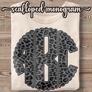 May include: A white t-shirt with a black and gray leopard print monogram in a scalloped circle. The monogram is the letters ABC.