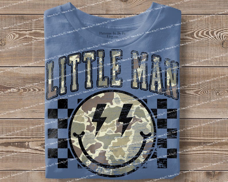 K&ouml;nnte beinhalten: Blaues T-Shirt mit dem Text "LITTLE MAN" in einer verblassten Schriftart. Darunter ein Smiley mit Camouflage-Muster und Blitzaugen, vor einem schwarz-wei&szlig; karierten Hintergrund.