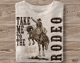 Może przedstawiać: Kremowy t-shirt z wytartą grafiką kowboja na dzikim koniu. Tekst "TAKE ME TO THE RODEO" jest wydrukowany w stylu vintage. Koszulka wykonana jest z miękkiego materiału.