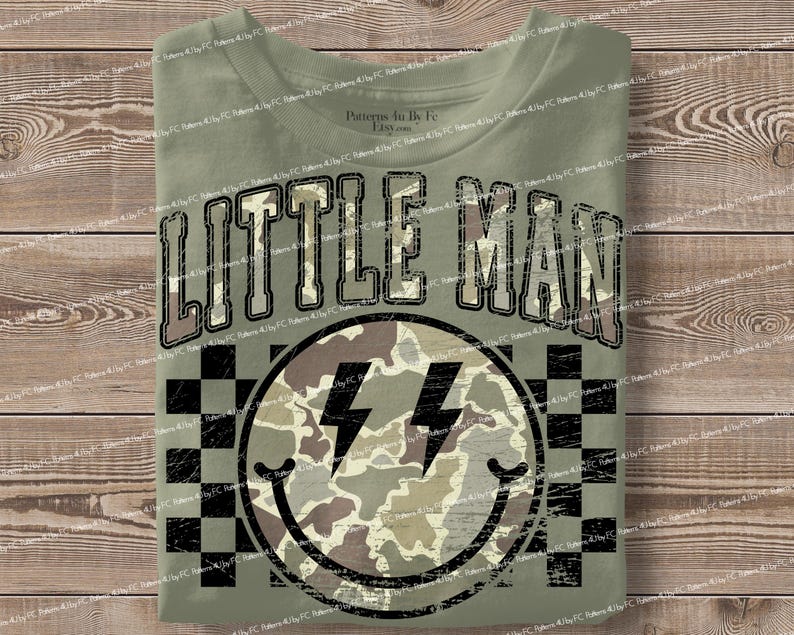 K&ouml;nnte beinhalten: Olivgr&uuml;nes T-Shirt mit dem Schriftzug "LITTLE MAN" in einer verwaschenen Schriftart. Darunter befindet sich ein Smiley mit Blitzaugen und einem Tarnmuster. Der Hintergrund hat ein schwarz-wei&szlig;es Schachbrettmuster.