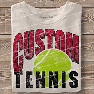 Puede incluir: Camiseta de color crema con las palabras "CUSTOM TENNIS" en rojo y negro, con un gr&aacute;fico de pelota de tenis verde. La camiseta tiene un aspecto desgastado.