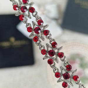 May include: A silver-toned bracelet featuring a repeating pattern of star-shaped and round red gemstones. The bracelet is composed of delicate chain links, with the gemstones adding a vibrant contrast to the metallic silver.