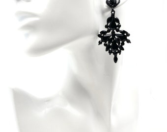 May include: Black chandelier earrings with multiple teardrop-shaped and oval-shaped black crystals. The earrings are attached to a black stud and are displayed on a white mannequin head.