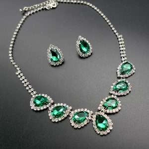 Puede incluir: Un conjunto de collar y pendientes plateados. El collar presenta piedras en forma de l&aacute;grima de color verde esmeralda, cada una rodeada de cristales transparentes m&aacute;s peque&ntilde;os. Los pendientes repiten el dise&ntilde;o con una sola piedra en forma de l&aacute;grima.