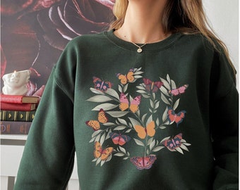 May include: A dark green sweatshirt with a graphic print of a cluster of butterflies and leaves. The butterflies are in shades of orange, pink, and purple.
