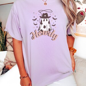 May include: A lavender t-shirt with a graphic of a ghost wearing a cowboy hat and a lasso. The text "Howdy" is printed below the ghost.