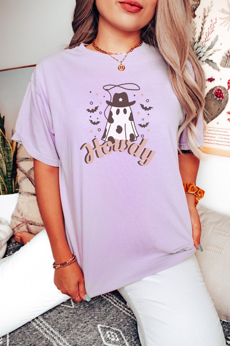 May include: A lavender t-shirt with a graphic of a ghost wearing a cowboy hat and a lasso. The text "Howdy" is printed below the ghost.