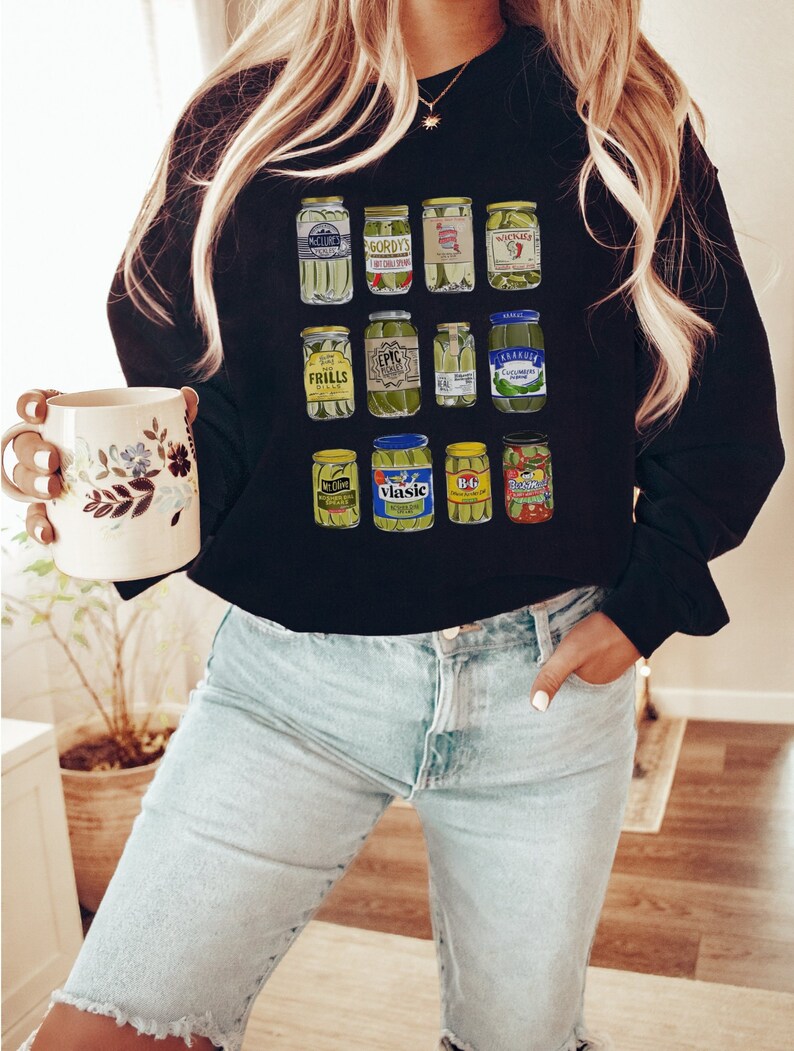 Op de afbeelding: Een zwart sweatshirt met een grafische print van verschillende augurkenpotten. De potten zijn in een rasterpatroon gerangschikt en tonen verschillende augurkenmerken, waaronder Gordy's, Vlasic en B&G.