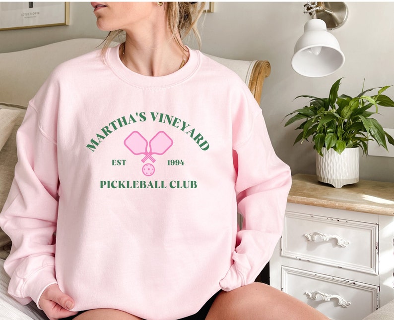 May include: Pink sweatshirt with a green graphic that says "Martha's Vineyard Est 1994 Pickleball Club" with a pink pickleball paddle and ball.