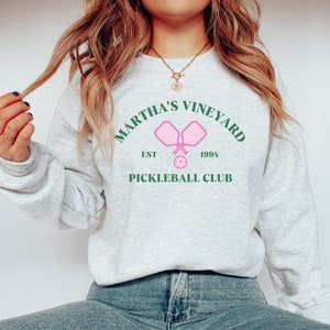 May include: A gray sweatshirt with a green and pink graphic design that says "Martha's Vineyard Pickleball Club" with the text "Est 1994" and two pink pickleball paddles.